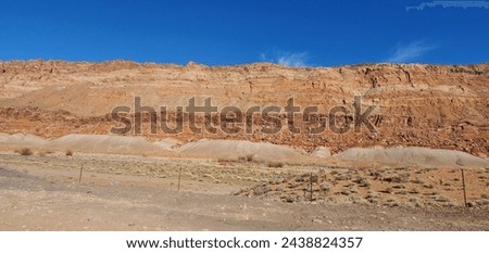 multi-colored striations of a mountain against a bright blue sky with wispy couds