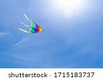 The multi-colored strips of a rainbow kite flies in the clear blue sky in the rays of the sun. The concept of a dream, freedom, childhood, tranquility, happiness, success. Background with copy space.