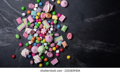 Multicolored Sweet And Bright Dragee, Candies, Lollipops, Marshmallows For Fun Party On Black Marble Background