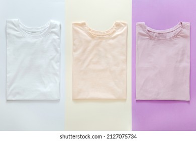  Multicolored t shirts pastel colors Pink White Purple Mockup for design on color background. Stacked Basic t shirts clothes trendy Minimalistic concept. T Shirts flat lay.