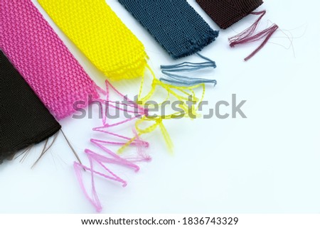 Multi-colored textile belts with threads sticking out on a white background. A strap tape that slips. The belt is unraveled with threads.