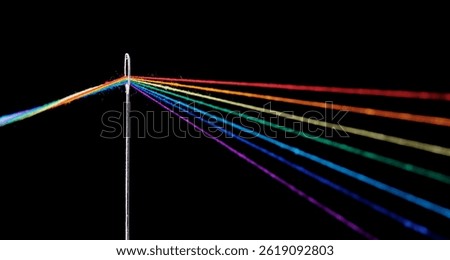 multi-colored threads for sewing in the form of a rainbow pass through an antique needle on a black background close-up