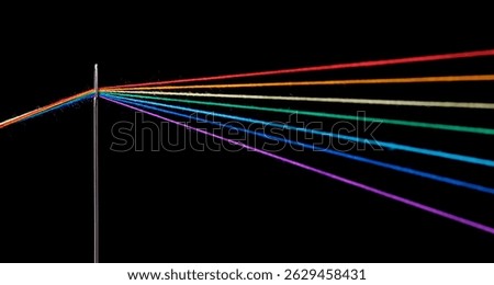 multi-colored threads for sewing in the form of a rainbow pass through an antique needle on a black background close-up