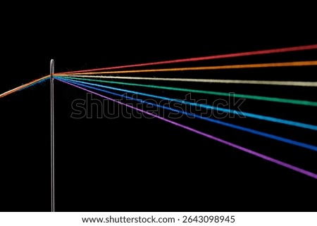 multi-colored threads for sewing in the form of a rainbow pass through an antique needle on a black background close-up