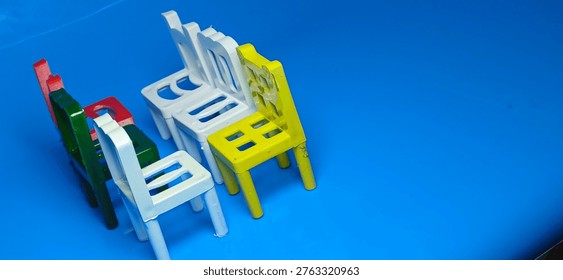 Multicolored tiny chairs aligned in perspective on blue reflective surface, minimal concept of waiting area, empty seats, playful classroom furniture design.