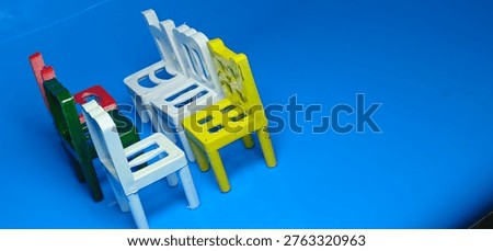 Multicolored tiny chairs aligned in perspective on blue reflective surface, minimal concept of waiting area, empty seats, playful classroom furniture design.