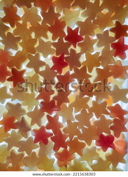Multi-colored transparent jelly candies in the\
shape of a star all over the background, brightly lit from below.\
View from above