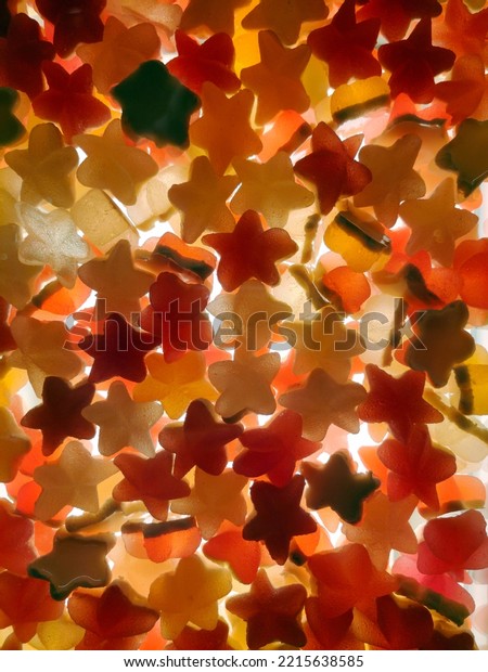 Multi-colored transparent jelly candies in the\
shape of a star all over the background, brightly lit from below.\
View from above