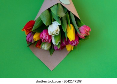Multicolored tulips are wrapped in craft paper. Place for text. Bouquet of tulips. Flower delivery. Green background . Tulip opy space. Spring concept. Copy space.