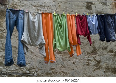 Multicolored washes are hanged up in the old town. Old loamy wall is background of this picture.