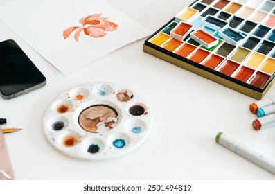 Multicolored watercolor palette, brush, colored pencils and equipment for painting on white desk - Powered by Shutterstock