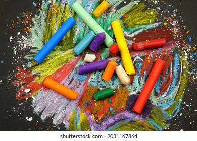 Multi-colored wax crayons lie on a black surface with chaotic crayon drawings on it