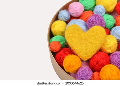 A lot of multi-colored wool balls of yarn with a yellow wool heart in a round cardboard box on a white background.Handmade concept, favorite hobby, thread sales.Rainbow layout of a needlework store.