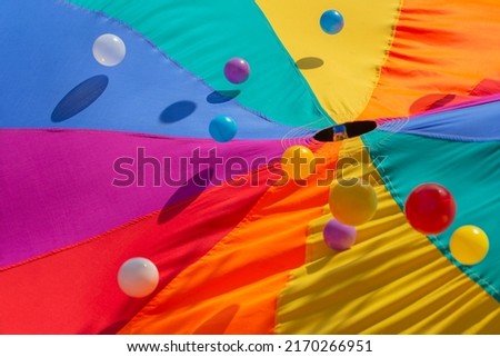 Multicolor-patterned kids play parachute with colorful bouncing balls. Rainbow colors toys for outdoor activities