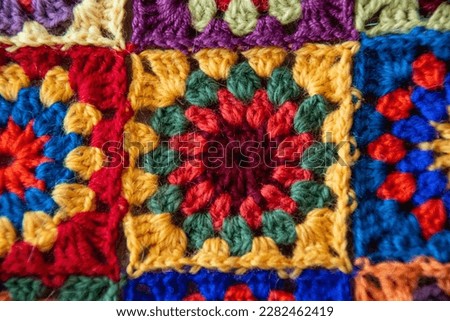 Multicolour square crocheted in maroon, red, green and yellow wool yarn. A beautiful multi-colored plaid is assembled from such squares. Crochet. Needlework. Handmade. Hobby.