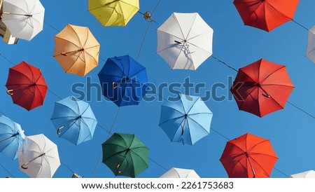 Multicoloured umbrellas hang in the street against a blue sky. Close-up. Urban street art. View from below. Interesting and beautiful decoration of the city