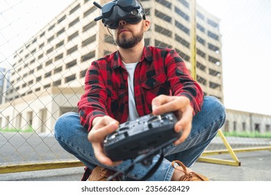 Multicopter racing competition. Close up portrait of casually dressed male fpv pilot operating drone using goggles nad remote controller.