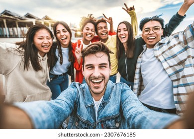 Multicultural best friends taking selfie pic with smart mobile phone outside - Laughing teenagers having fun on city street - Life style concept with guys and girls hanging out together  - Powered by Shutterstock