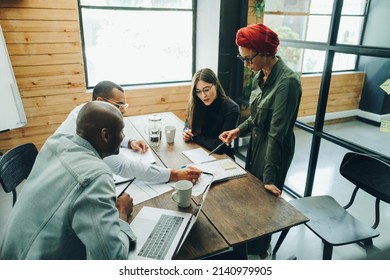 Multicultural Business Team Discussing A Report Document During A Boardroom Meeting. Group Of Creative Businesspeople Sharing Strategic Ideas In An Inclusive Workplace.