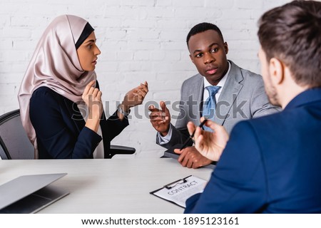 multicultural businesspeople gesturing while discussing contract near interpreter, blurred foreground