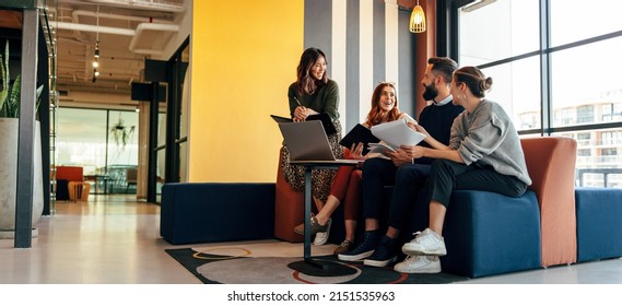 Multicultural businesspeople working in an office lobby. Group of happy businesspeople smiling while sitting together in a co-working space. Young entrepreneurs collaborating on a new project. - Powered by Shutterstock