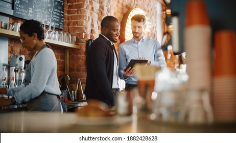 Multicultural Coffee Shop Owners Meeting Behind the Counter and Working on Tablet Computer and Checking Inventory in a Cozy Loft-Style Cafe. Successful Restaurant Managers and Barista at Work. - Powered by Shutterstock