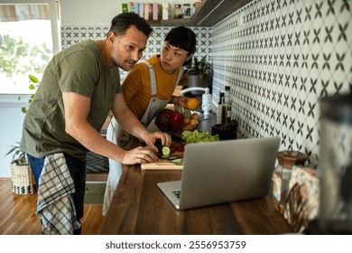 Multicultural couple cooking together while following a recipe on laptop in stylish kitchen - Powered by Shutterstock