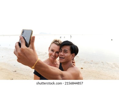 Multicultural Couple Embracing While Taking Selfie Stock Photo