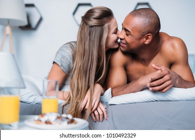 multicultural couple kissing and lying on bed