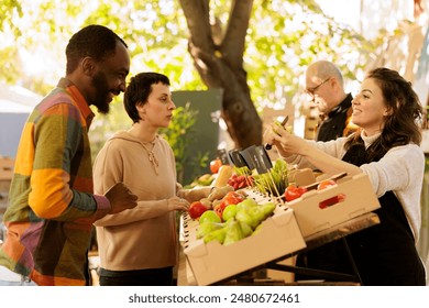 Multicultural couple man and woman purchasing seasonal natural produce at farmers market, looking at bio products. Smiling vendor standing behind fruits and vegetables stand, selling healthy food. - Powered by Shutterstock