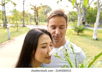 Multicultural Couple Smelling Tropical Flowers In An Urban Park