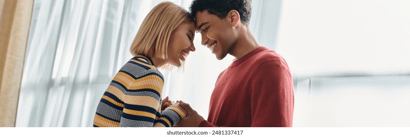 A multicultural couple smiles brightly at each other in their modern apartment. - Powered by Shutterstock