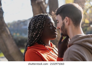 multicultural couple of sweethearts in engaging moment with an African woman touching tenderly her boyfriend chin under the trees in the park