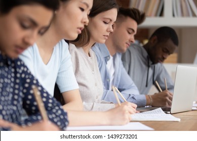 Multicultural diverse students sit at shared desk making notes studying together at university, multiethnic mixed school group write listen to tutor teacher talk giving lecture at college or school