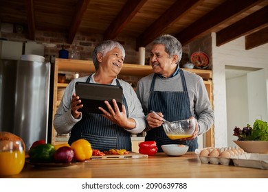 Multi-cultural elderly couple laughing together while cooking breakfast in modern kitchen, using tablet to research healthy recipe. - Powered by Shutterstock