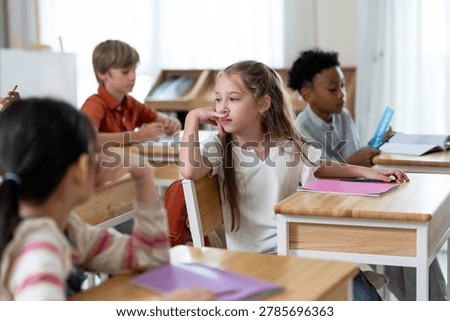 Multicultural elementary student group listens around wooden desk during first day classroom discussion, building friendship, attention, participation, learning routine, confidence in primary.