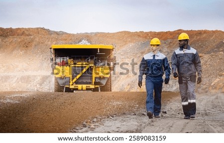 Multicultural Engineers work in open pit mine with mining truck in background.