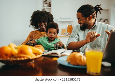 A multicultural family sitting together at the breakfast table at home. A diverse mother is playing with he son while his father, a remote worker, is working on a laptop online and laughing at them. - Powered by Shutterstock