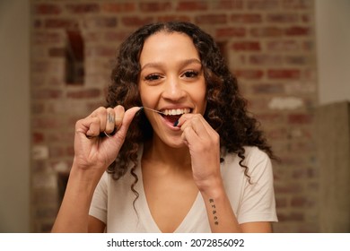 Multi-cultural female smiling while flossing her teeth in the mirror. Modern bathroom.