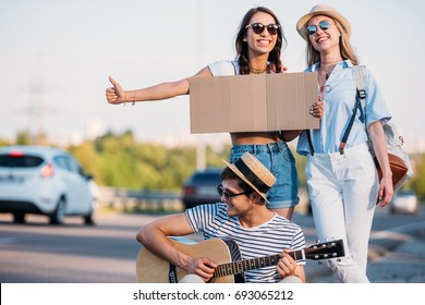 multicultural friends with empty cardboard hitchhiking while traveling together