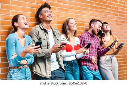 Multicultural friends laughing using smartphone at wall on university college campus - Young people addicted by mobile smart phones - Technology concept with always connected milenials - Vivid filter - Shutterstock ID 2045618270