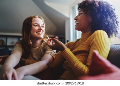 Multicultural gay women talking cheerful sitting on the couch - Couple of young lesbian girls having fun at home