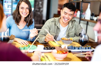 Multicultural gen z friends eating sushi with chopsticks at fusion restaurant winery - Food and beverage life style concept with happy people having fun together at eatery bar - Bright vivid filter
