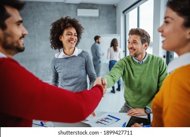 Multicultural group of business people having meeting in boardroom. Mature businessman shaking hands with his new young colleague.