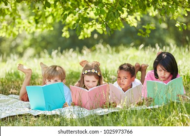 Multicultural Group Of Children Reading While Studying In The Park In Summer