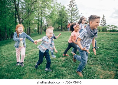 A Multicultural Group Of Children Running On The Grass Holding Hands. The Concept Of Childhood, Friendship, Intercultural Communication. Full Length