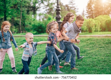 A Multicultural Group Of Children Running On The Grass Holding Hands. The Concept Of Childhood, Friendship, Intercultural Communication. Full Length