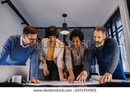 A multicultural group of engineers pointing at plans and blueprints at meeting room on a briefing.