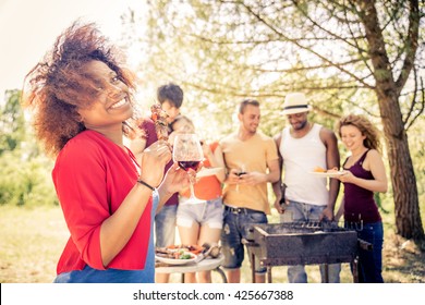 Multicultural group of friends grilling and having party in the backyard - Barbecue outdoors, cheerful people cooking meat and drinking wine