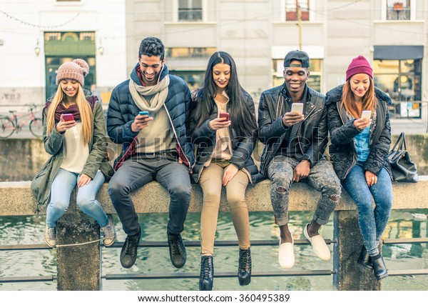 Multicultural group of friends using cellphones - Students sitting in a row and typing on the smartphones